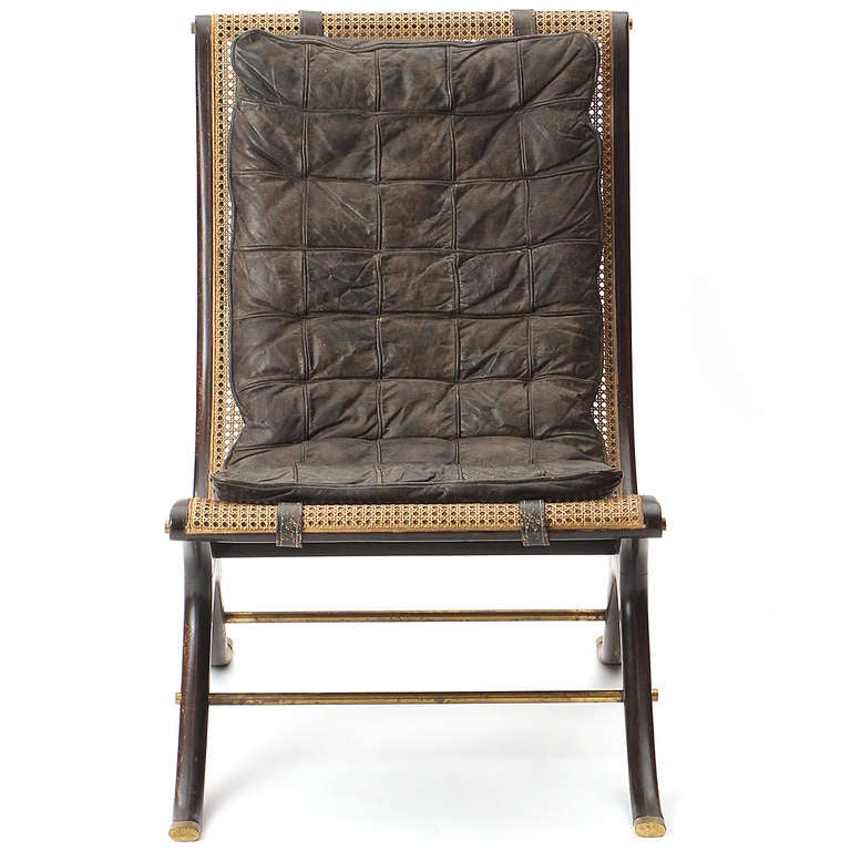 A dramatic and unusual x-framed scoop chair having a sculpted and lacquered mahogany frame, caning with a channeled leather cushion, and warm brass details including the stretchers and sabots.