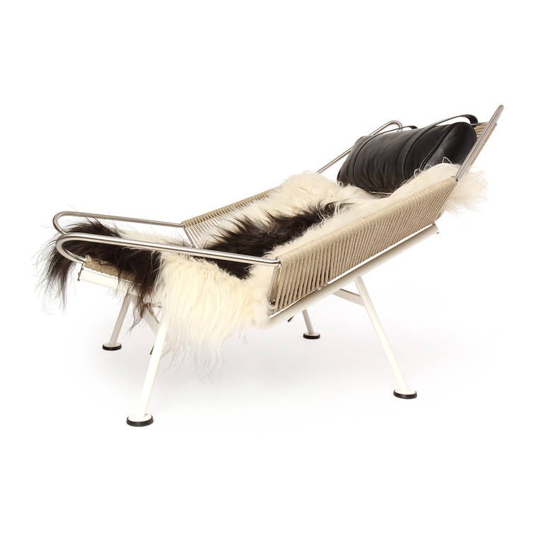 An iconic and dramatic lounge chair having a sculptural and engineered stainless steel frame with a seat and back made of plaited flag halyard. Comfort is added with a longhaired sheepskin throw and an adjustable leather headrest.