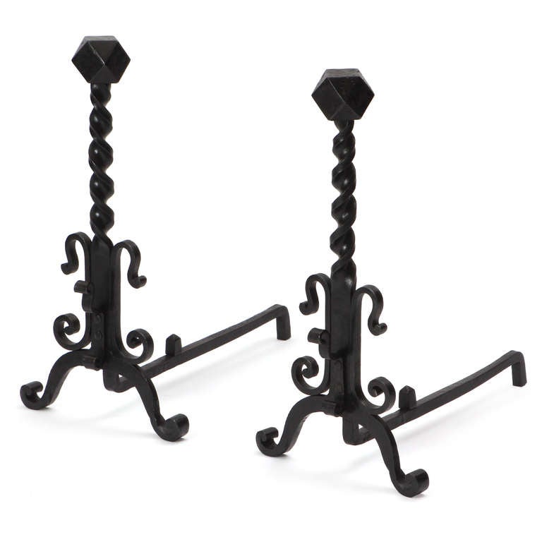 Blackened wrought iron andirons having an elaborate scrolling and twisting structure capped by an unusual faceted polyhedron.