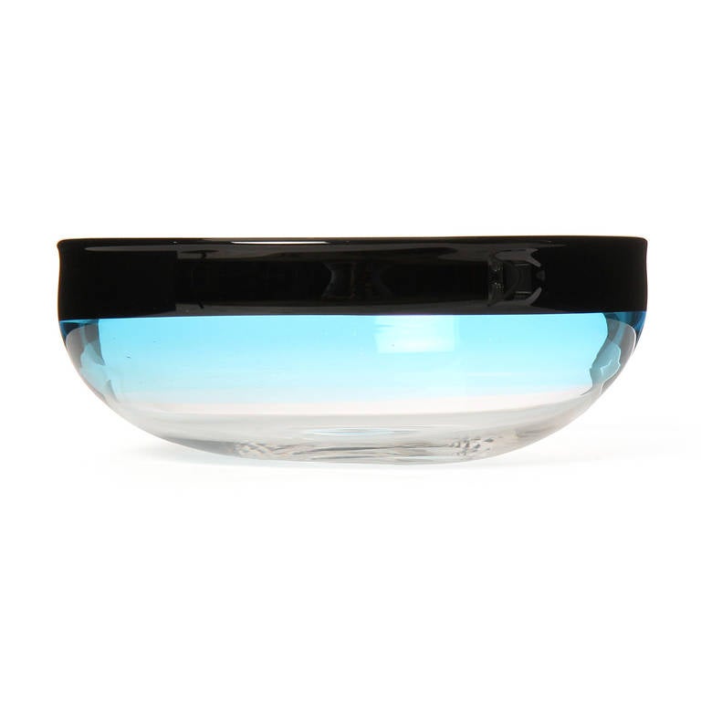 A finely proportioned hand blown glass bowl rendered in a luminous pale blue with a dark overlay on the rim.