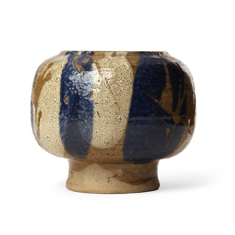 A masterfully hand thrown footed stoneware vase having a rich, rustic variegated glaze and a distinctive flattened top with a unique sculptural opening.