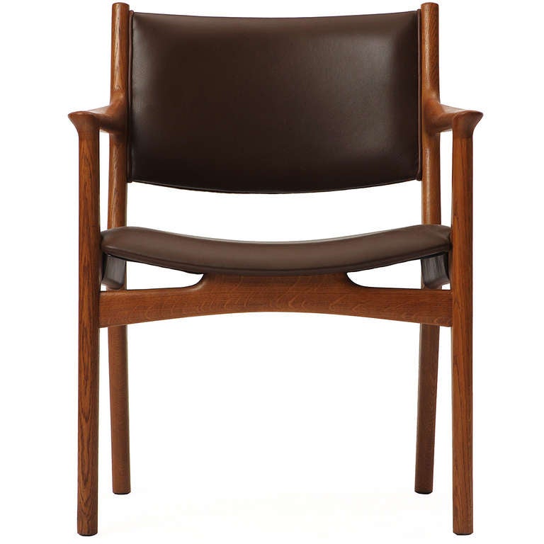 Un fauteuil en chêne avec une armature apparente, un siège et un dossier légèrement incurvés et recouverts de cuir.