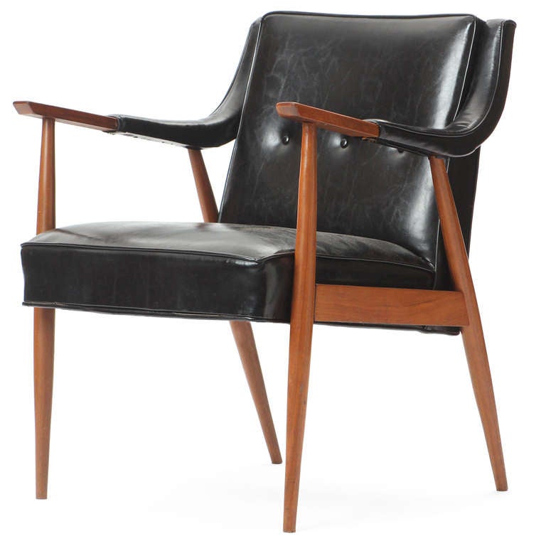 An expressive and comfortable arm chair having a sculptural walnut frame and leather-clad sloping arms, and button-tufted black leather upholstery.