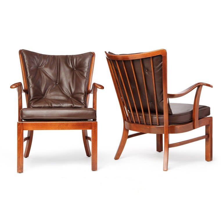 A fine pair of generously scaled open armchairs in mahogany having curved, slatted backs, sculpted cantilevered arms and fitted chocolate brown oiled leather upholstery.
