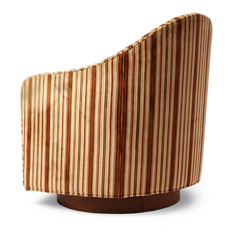 A swiveling lounge chair by Milo Baughman having a sculptural body resting on a walnut disc base, retaining its original vibrant striped upholstery. Produced by Thayer-Coggins in the USA, circa 1960s.