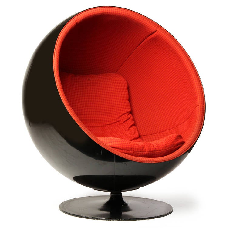 An iconic and expressive swiveling Ball lounge chair, the black fiberglass spherical seating element having bold red upholstery and floating above a pedestal base.