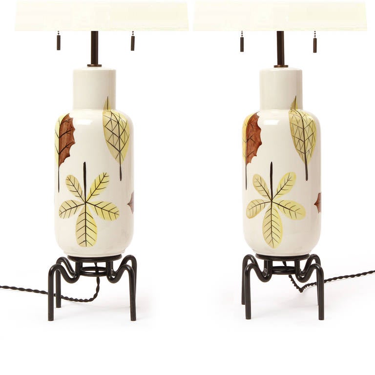 A delightful and graphic pair of ceramic table lamps having hand painted foliate decoration and expressive sculptural metal bases.