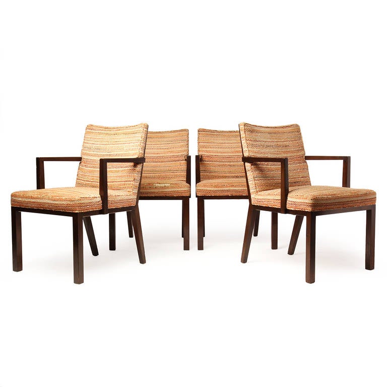 A set of four (4) elegant and generously proportioned dining chairs with wooden panel backs, having spare, square-legged mahogany frames and tailored, form fitting upholstery.