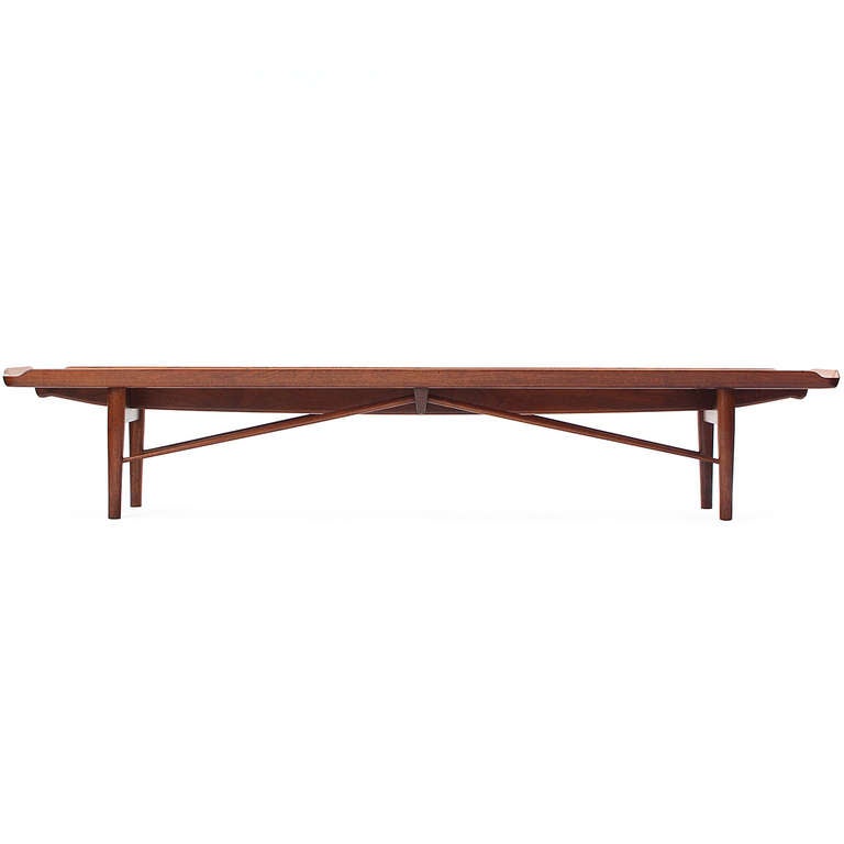 An uncommon and expressive long and low bench or low table in walnut having angled architectural bracing supports and an elegant top with raised edges and three inset planks set at right angles to the grain.