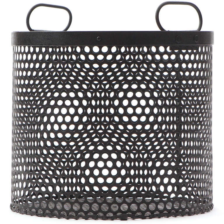 An interesting and well-constructed industrial circular handled basket made of patinated and perforated steel. The perforated surface creates a dynamic visual effect when looked through.