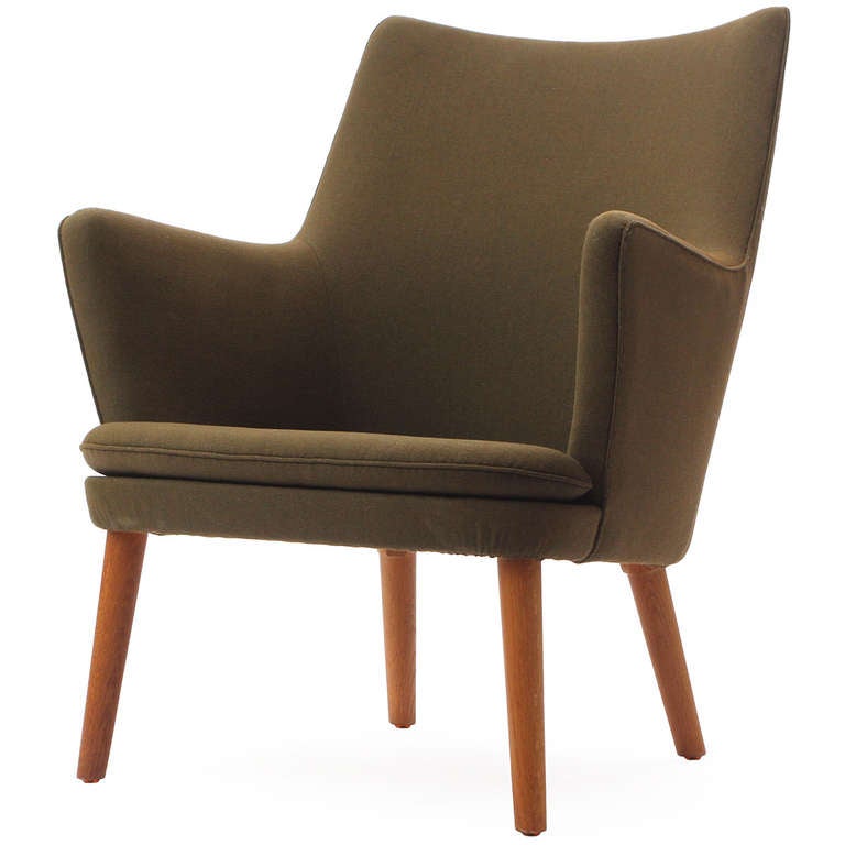 A lounge armchair with a tight upholstered back and loose seat cushion that sits on solid teak tapered dowel legs, retains the original green wool upholstery.
 