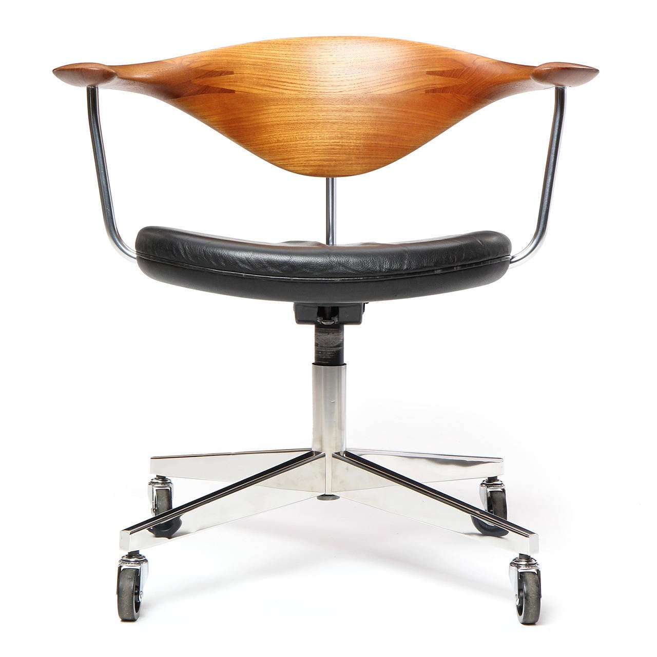 A magnificent swiveling desk chair having a hand-sculpted suspended teak backrest and black leather upholstery, the seat floating on a chromed steel base with casters. A masterpiece of Danish modernism designed by Hans Wegner and crafted by