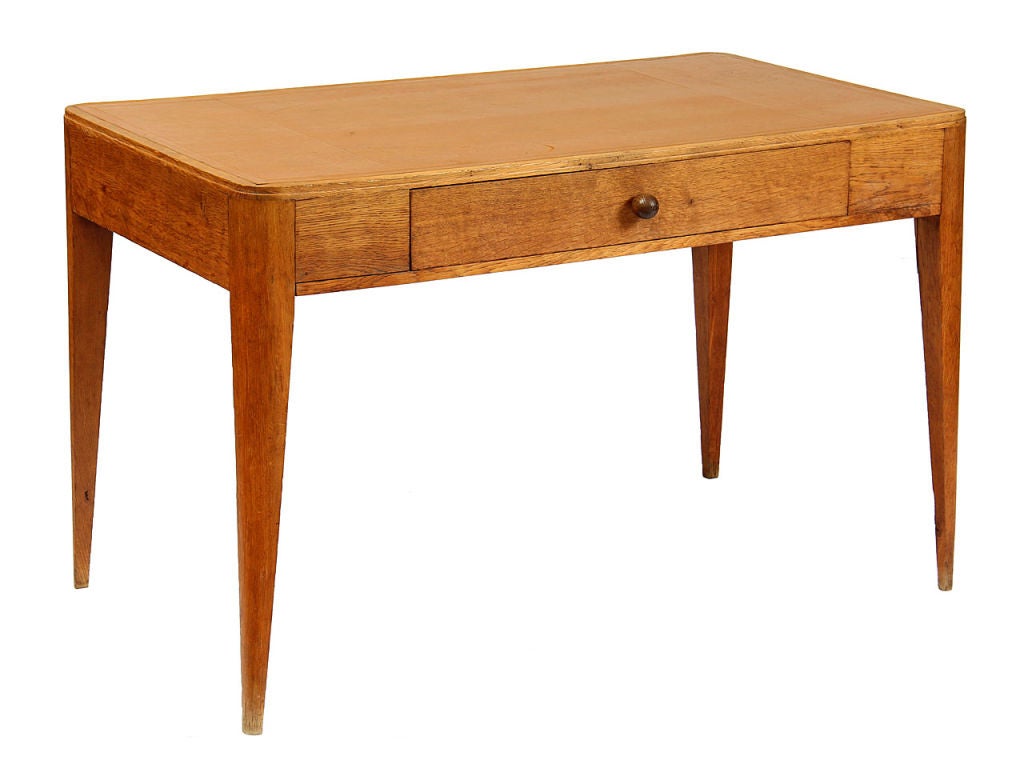 A rectangular oak desk with rounded corners, a tan leather writing surface and a central drawer, on tapered legs.