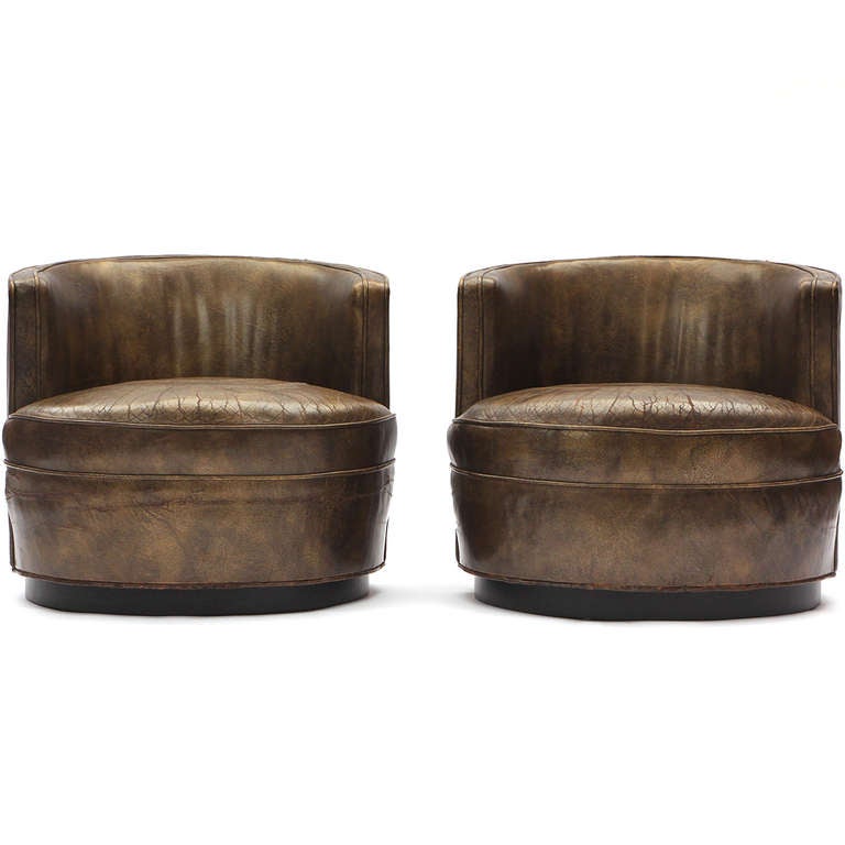 A rare and elegant pair of swiveling barrel-back lounge chairs fully upholstered in beautifully aged olive-brown leather.