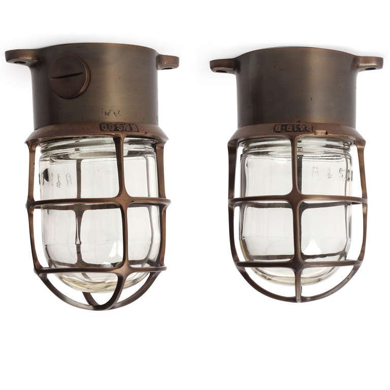 A great quality industrial ceiling or wall, light fixture in patinated bronze with a thick clear glass cage-encased light diffuser.