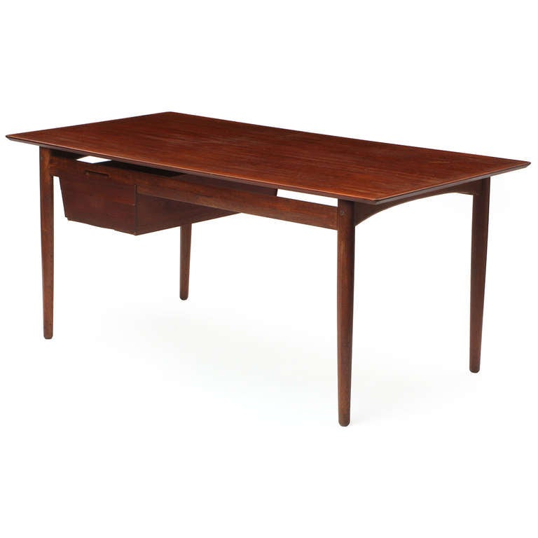 A writing desk finely crafted in solid teak having a floating bank of drawers and turned dowel legs.