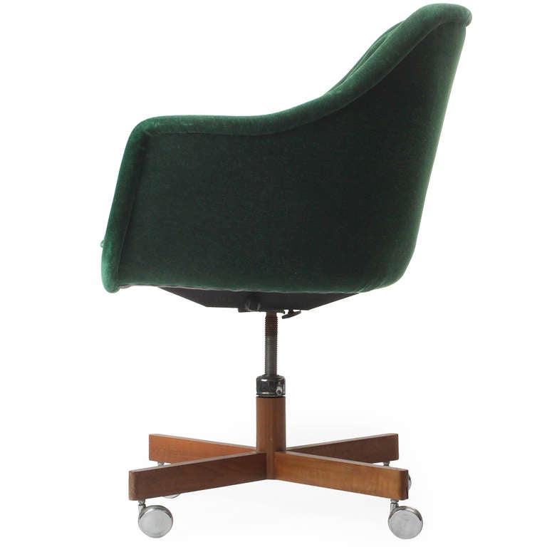 An expressive and comfortable swiveling and adjustable desk chair retaining its original emerald tufted upholstery and floating above a walnut cruciform base on casters.