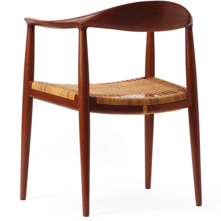 A teak 'Round' chair with masterfully sculpted backrest and arms floating atop tapered dowel legs having a caned seat.  This sublime chair became known as 'The Chair'.