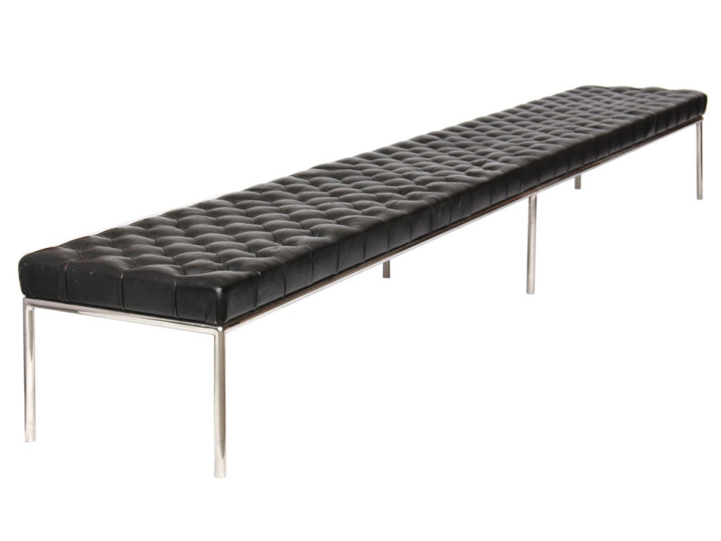 An oversized tufted black leather bench with a chromed solid rod base.