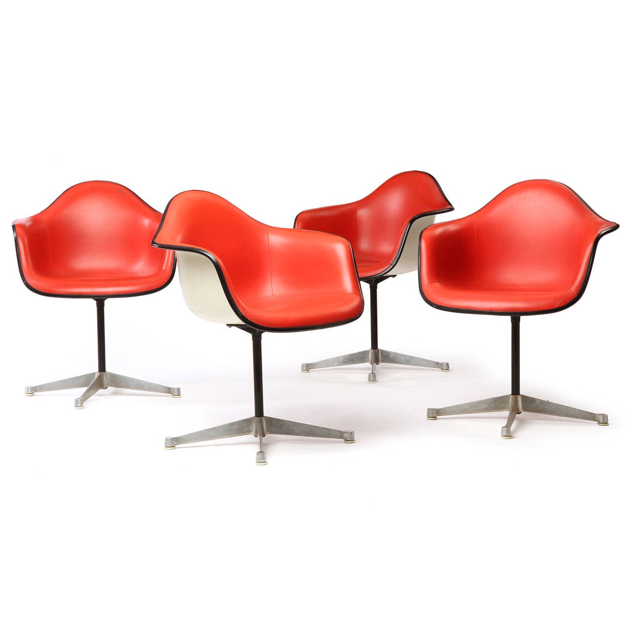 A vibrant group of swiveling armchairs having organically shaped seats with their expressive original red upholstery floating on lacquered stems rising from early four-pronged bases.