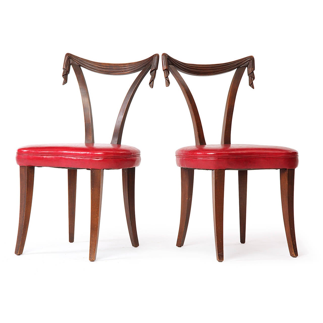 An elegant pair of occasional chairs having open backs with dramatic hand-carved draped and scrolling top rails and expressive seats of cherry red Naugahyde.