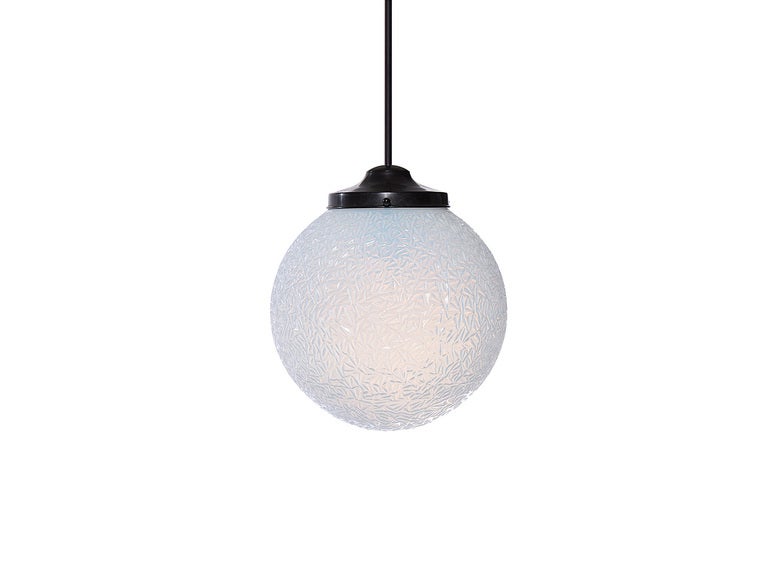 A ceiling fixture with a patinated brass canopy and stem supporting an opalescent, crinkled glass globe.