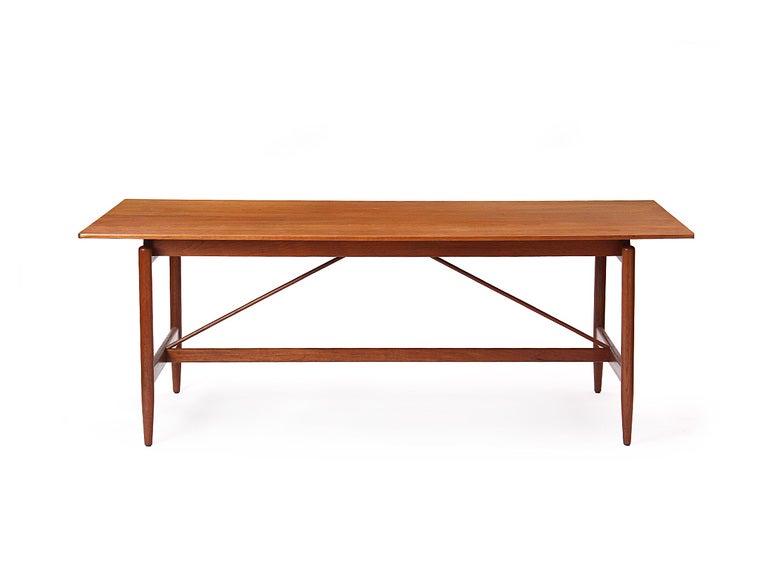 A teak library or dining table with tapered dowel legs, a long stretcher and angled support braces.