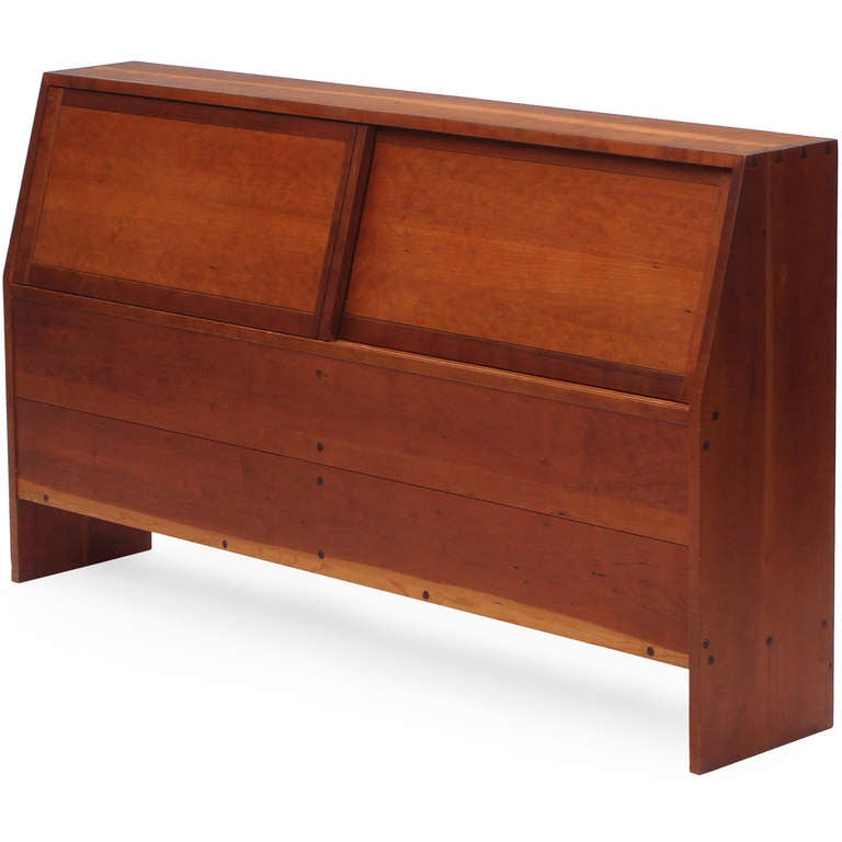 A queen size American craftsman headboard by George Nakashima featuring bench made solid cherry wood construction with dovetailed joinery. Two sliding doors opening to a storage compartment. Made by George Nakashima Studio in the USA in the 1950s.