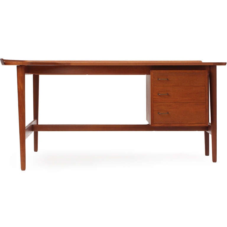 A fine desk in teak having an architectural exposed frame, suspended three (3) drawer cabinet and a boomerang-shaped top with a raised and curved rail.