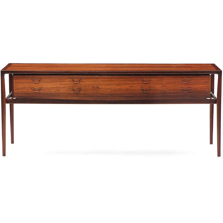 A refined and elegant cabinet-made console/cabinet/sideboard in highly figured rosewood having a sculptural frame encasing a floating bank of drawers with handlebar brass pulls.