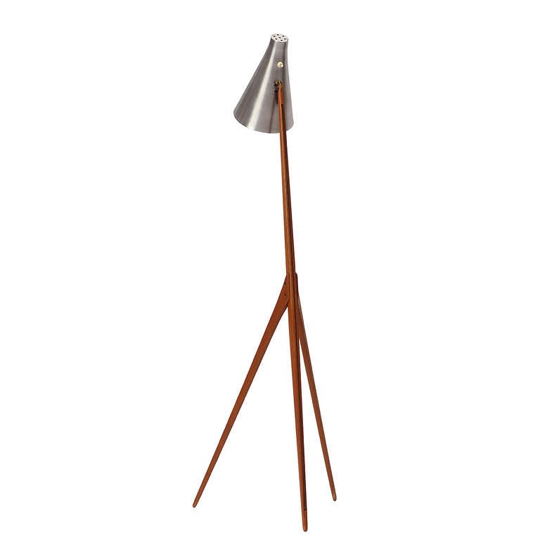A sculptural and elegant floor lamp in teak having a sleek three pronged base supporting a swiveling uncolored aluminum visor.