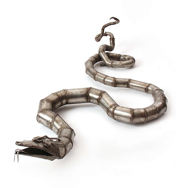 A wall mounted sculpture of a large serpent made of welded steel pipe and other steel parts.