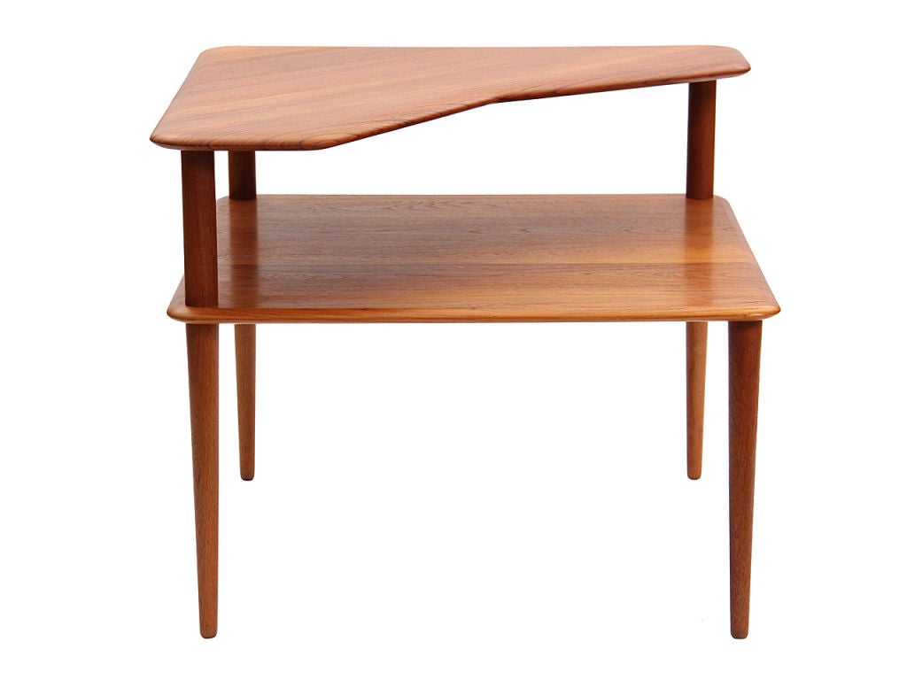 A two-tiered end table in solid teak with a cut-away top shelf.<br />
Designed by Hvidt and Molegaard for France and Sons