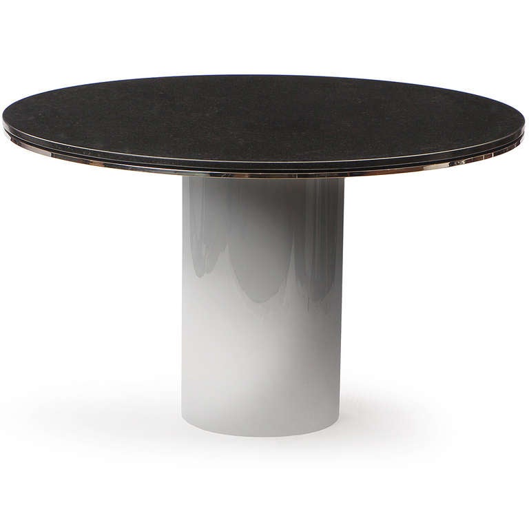 A minimal and dramatic pedestal table fashioned from a stainless steel cylinder form supporting a round black granite top with steel banding inset into the edge.