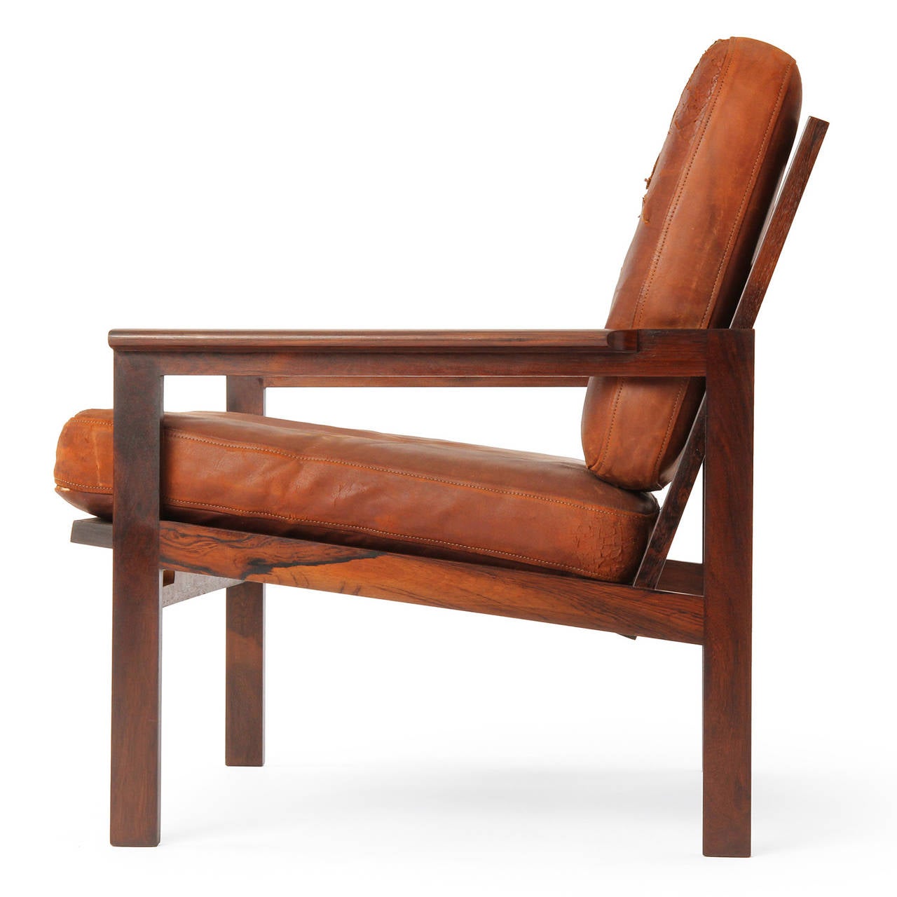 Ce fauteuil rectiligne de style scandinave moderne, conçu par Illum Wikkelso, présente un cadre en bois de rose massif apparent, de larges accoudoirs aplatis et des coussins en cuir naturel à la patine magnifique. Fabriqué par l'ébéniste Neils