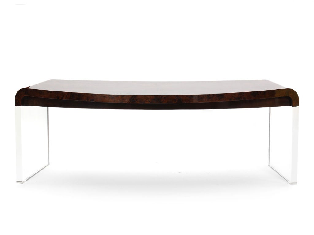 A crescent-shaped burled walnut desk with a central drawer and lucite slab supports.