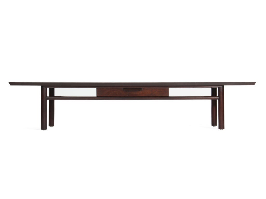 An ebonized mahogany low table with a lower shelf and singe drawer on cylindrical dowel legs.
