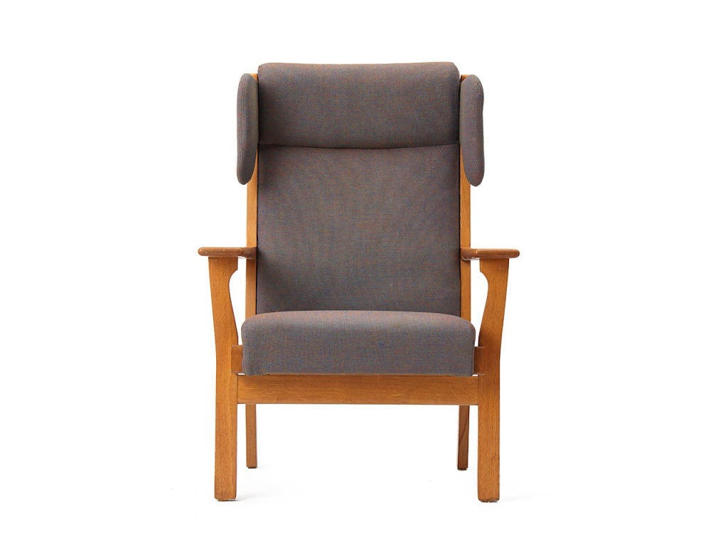 A wingback lounge armchair with a teak frame, retaining the original grey wool upholstery.