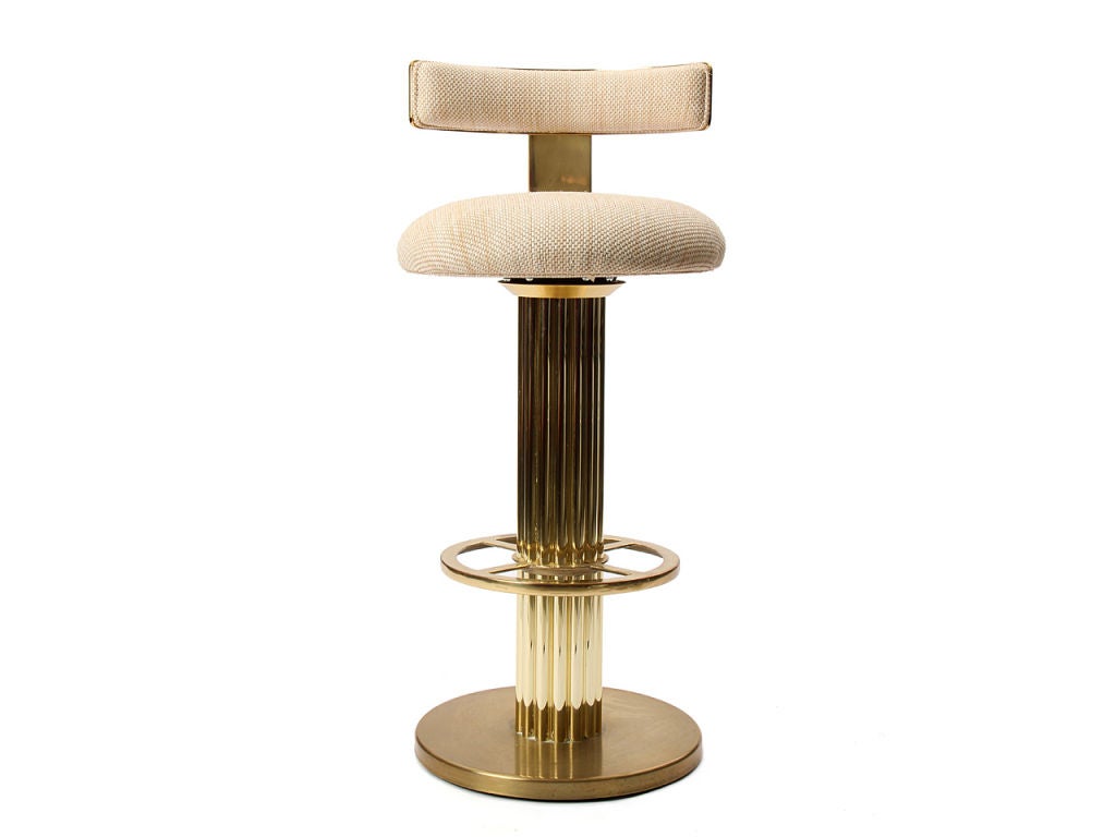 A pair of brass plated barstools with a reeded column and upholstered swivel seat and back.