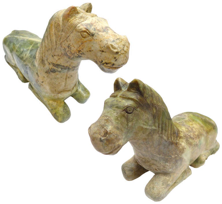A decorative pair of sitting horse statues in jade onyx.  These elegantly carved, architectural animals, though very similar in pose and execution, present their own distinct personalities. Likely Asian in origin, this lovely pair will add strong