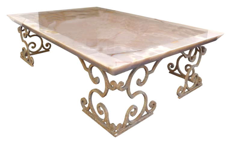 A coffee table of extraordinary scale in onyx and wrought-iron.  A massive slab of coral onyx, reverse-beveled, affixed to stylized, Spanish-revival wrought-iron legs wearing an even, applied patina.  A wonderful juxtaposition of minimalist