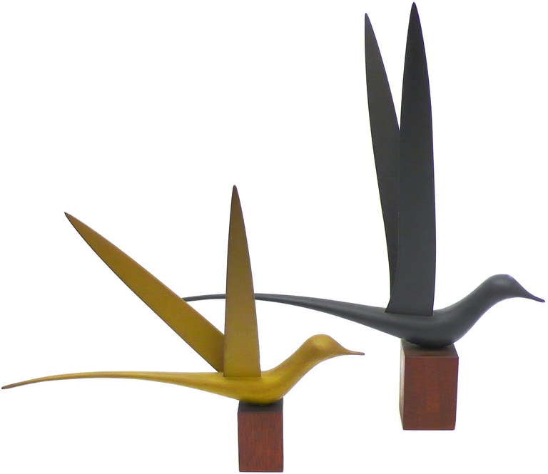 A pair of beautifully stylized, delicately hand-carved wooden bird sculptures hand-painted in warm, wonderfully muted, matte tones of mustard and gunmetal.  Mounted to their original mahogany bases, these whimsical forms proudly imply elegant motion