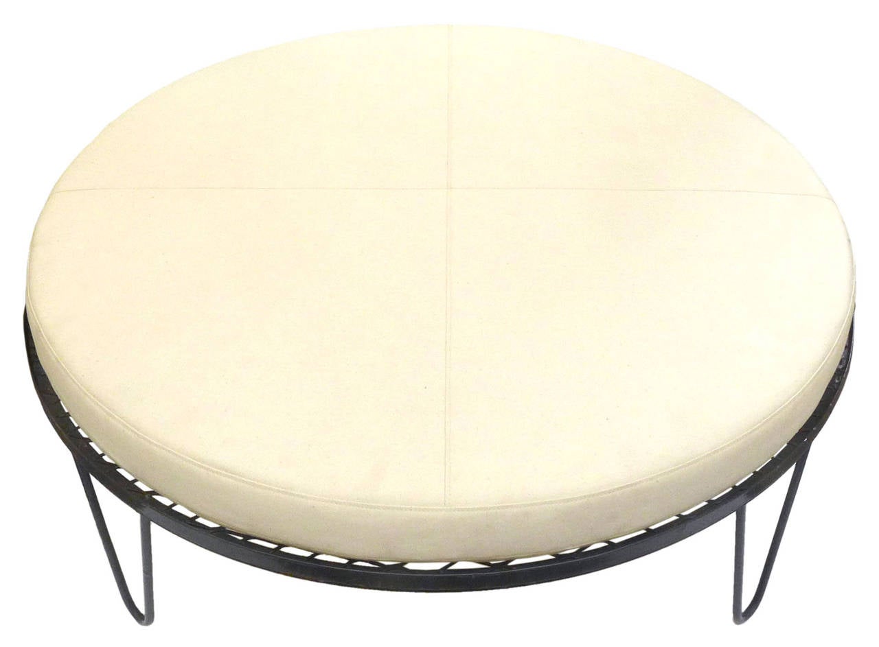 An attractive and unusual wrought iron and canvas ottoman. A simple form of an inviting, atypically-ample, round surface atop four, graceful, hairpin legs. Great scale and proportions with potential as an ottoman, low seating or coffee table. Item