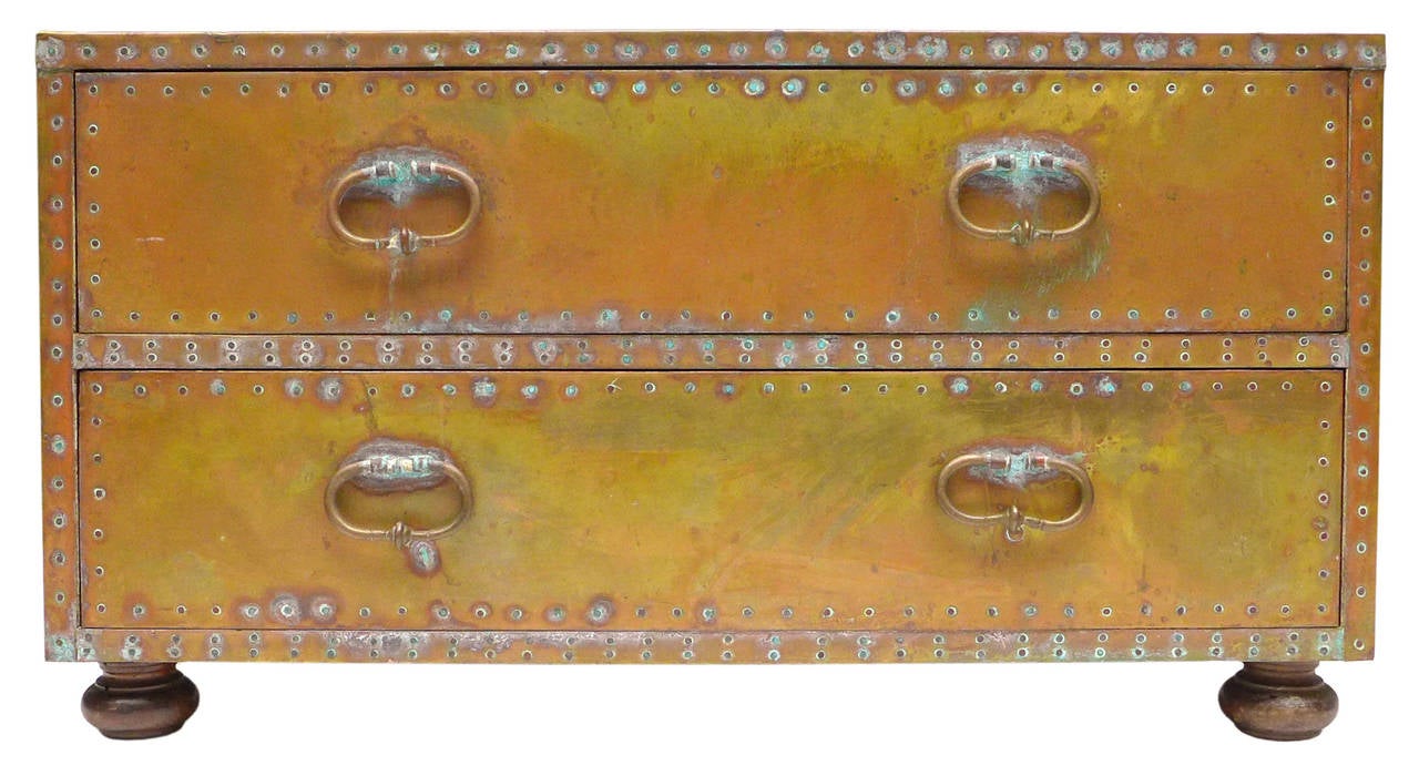 An exceptional, low brass-clad two-drawer chest by Sarreid. A fantastically mottled and oxidized patina with a warm blend of surface tones creating magnificent decorative character. All original handles and turned wood doughnut feet. One of the