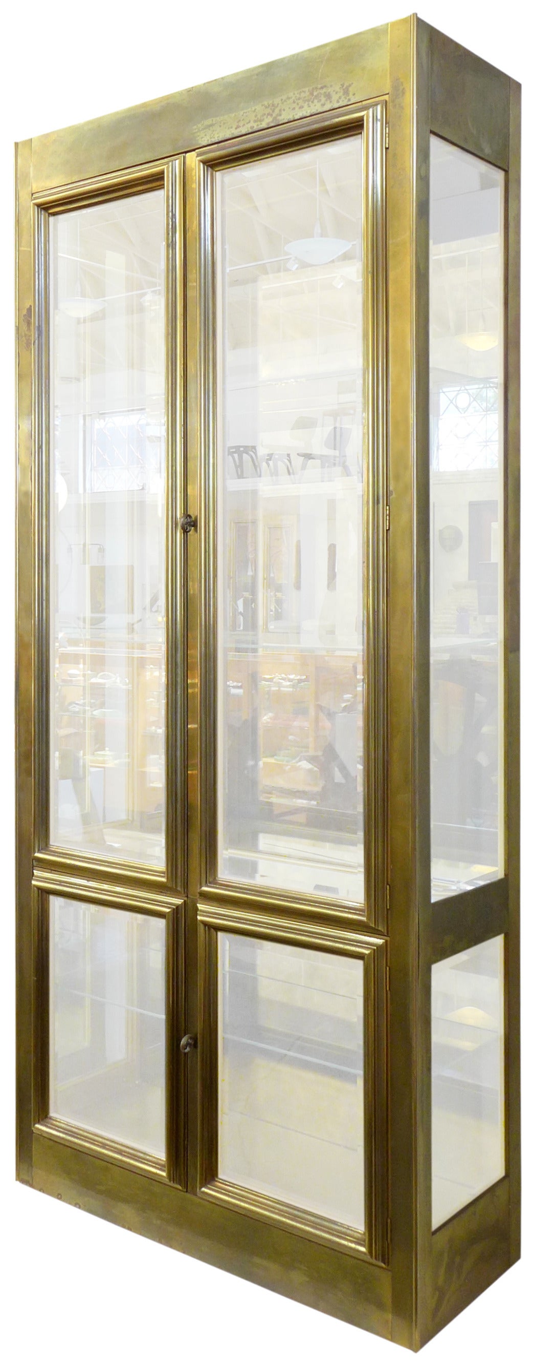 A large and impressive, brass-clad display case by Mastercraft. A striking, monolithic form elegant in every detail: Adjustable glass shelves, mirrored back, two overhead lights and graceful frame details on the door-fronts. A much-desired patina