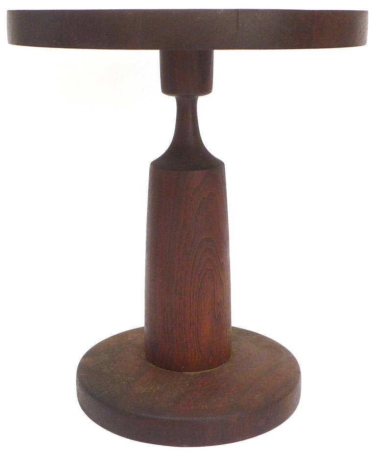 A beautiful teak side table by Paul A. Tarantino (1927 - 2014).  A turned-wood pedestal-leg with a laminated, round top and plinth.  A modernist and sculptural form with clean lines in an organic medium.  Tarantino studied at Cranbrook Academy of