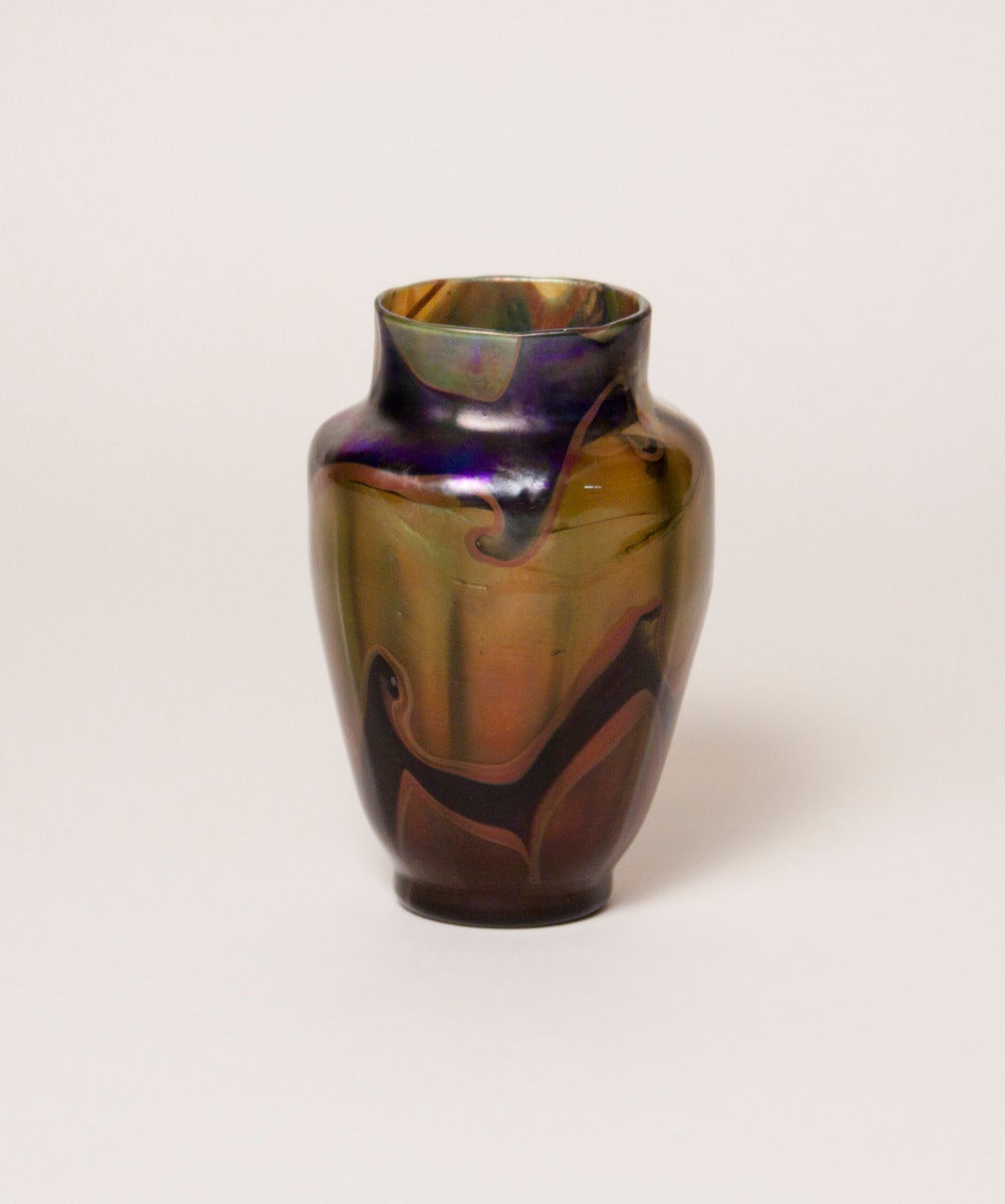 An exceptional example of the innovative glass techniques used at Tiffany Studios during the early years of production, this Tiffany favrile glass reactive paperweight vase dates from the late 1890s. The vase features swirling iridescent hooked