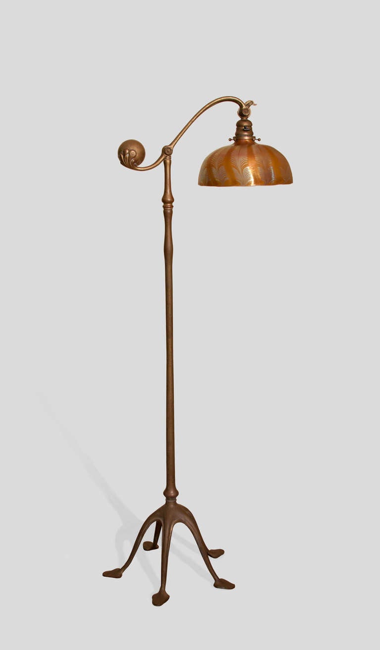 A Tiffany Studios bronze and Favrile glass balance weight floor lamp comprising a five-footed gilded bronze base with an amber damascene cased blown glass shade decorated with silvery blue iridescent feather design.