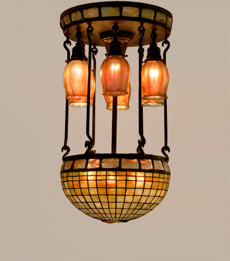 A Tiffany Studios hanging fixture featuring six favrile glass shades and an inverted hanging shade with turtle back glass border. The fixture has its original metalwork and can be mounted flush to the ceiling.