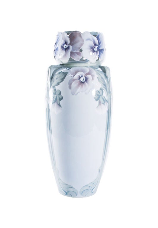 A monumental porcelain Rorstrand vase modeled with pansies. The tall cylindrical form has a waisted neck with a rim modeled as open-face pansies, with flowering stems flowing down the white ground body of the vessel.